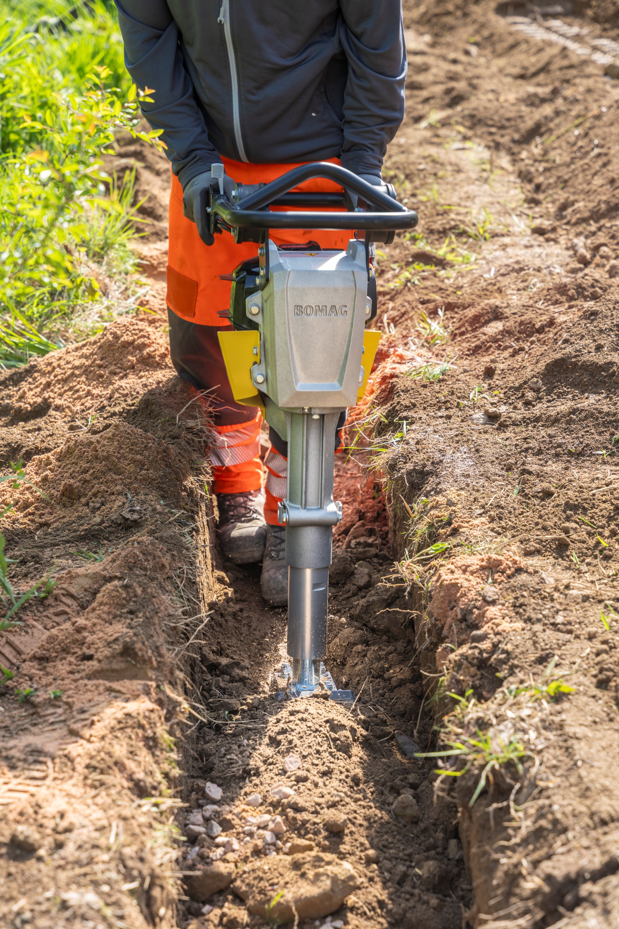 Construction worker operating a Bomag jackhammer to dig a trench in soil