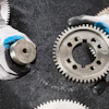 Industrial metal gears with blue-tipped work gloves on textured surface