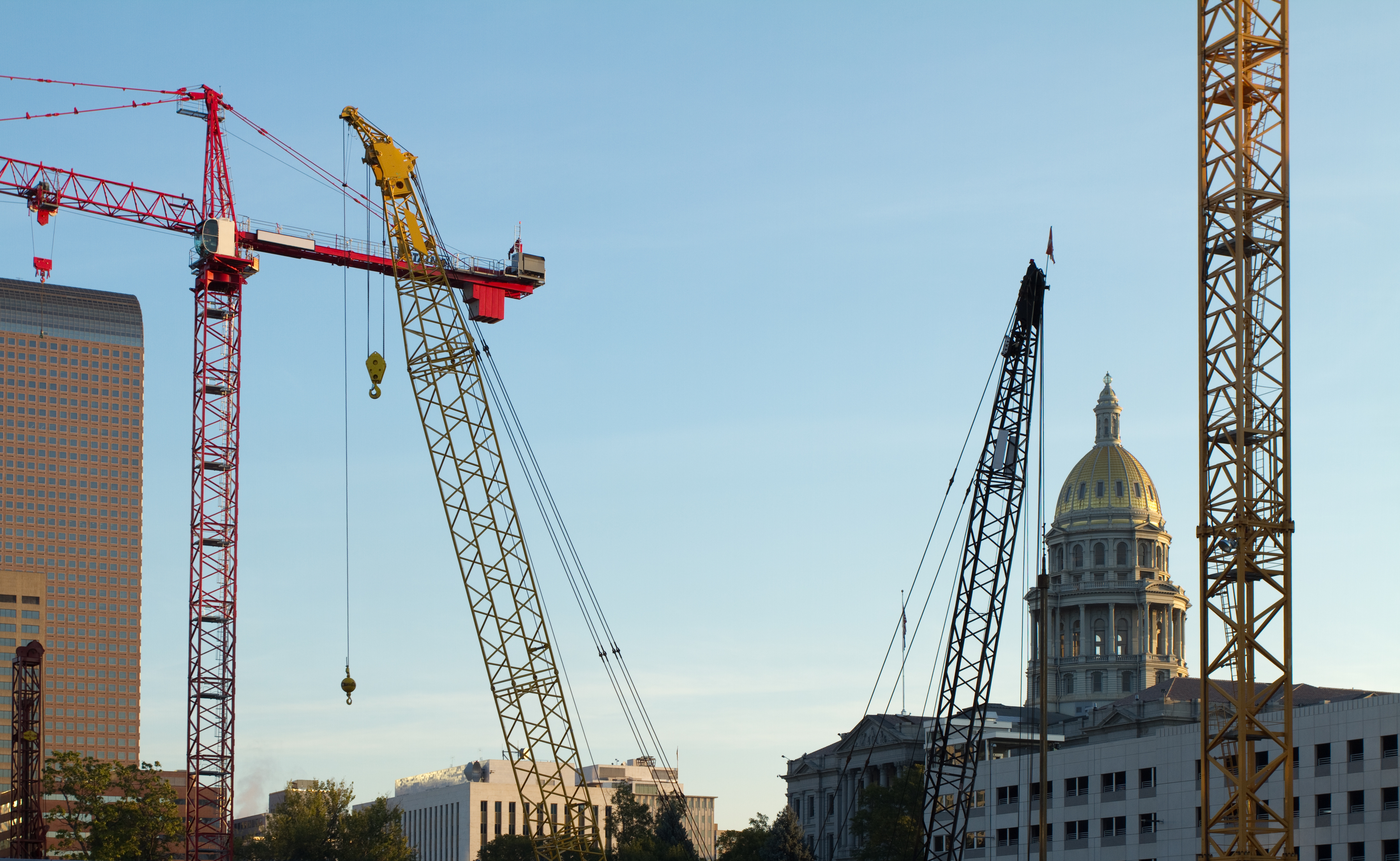 Construction cranes near state capitol building with golden dome under blue sky