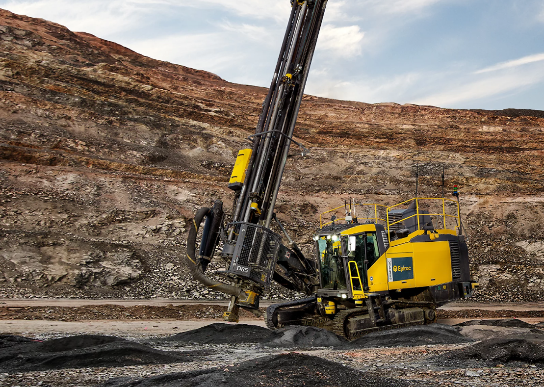 Yellow crawler drilling rig operating in rocky open-pit mining terrain