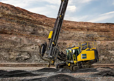 Yellow crawler drilling rig operating in rocky open-pit mining terrain