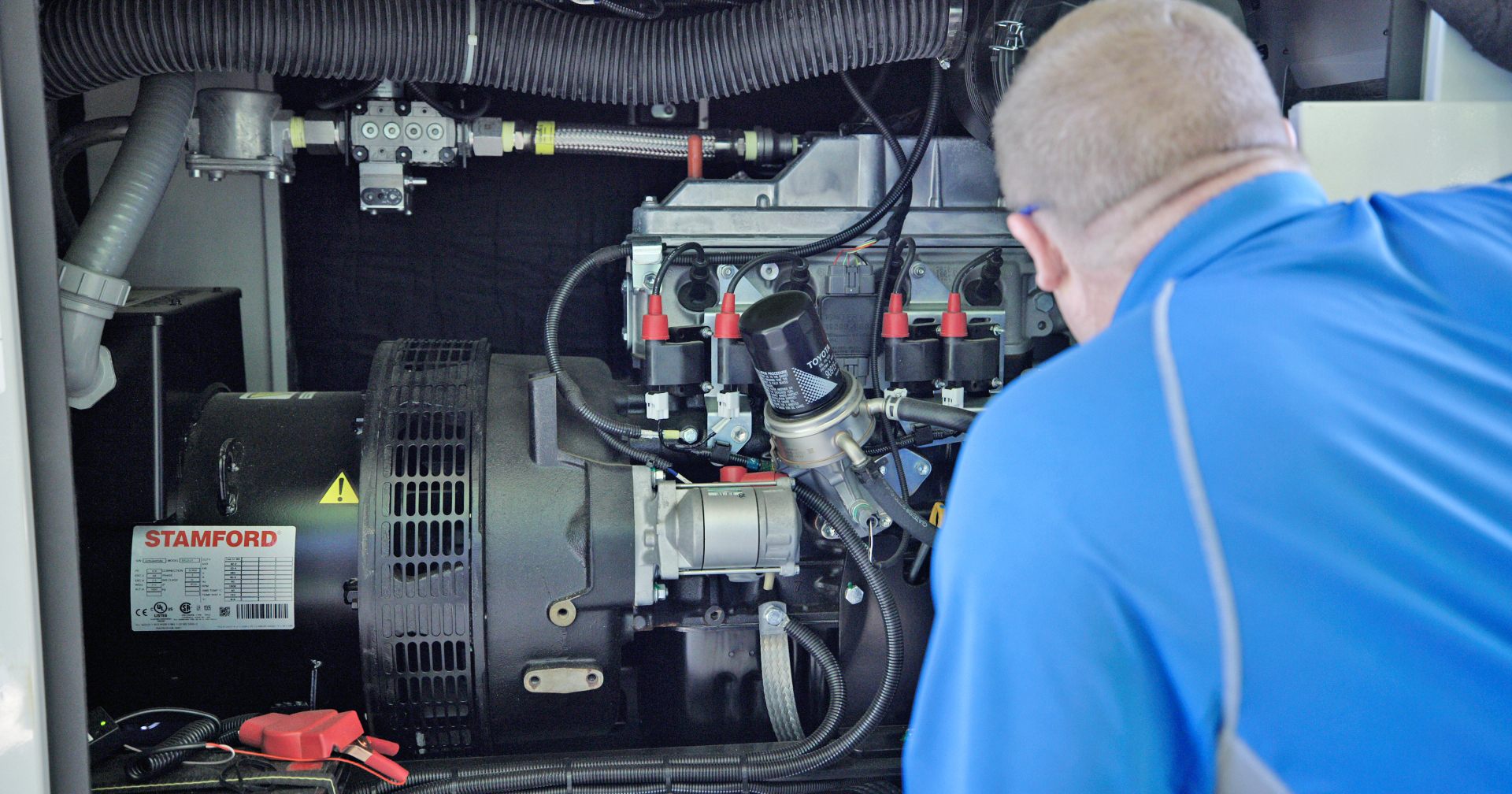 Technician inspecting industrial electrical generator with complex mechanical components