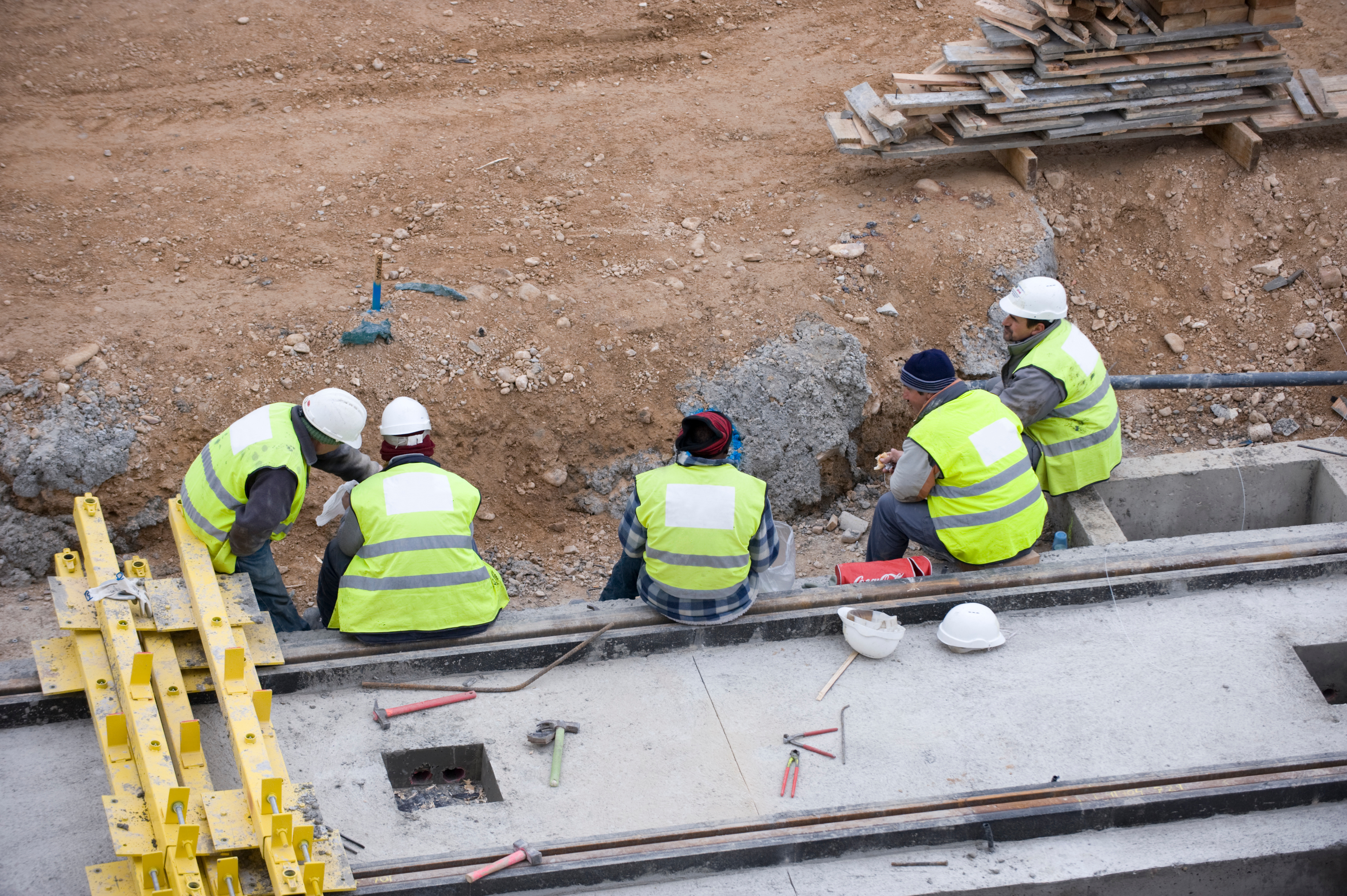 Construction workers in high-visibility vests examine site foundation work