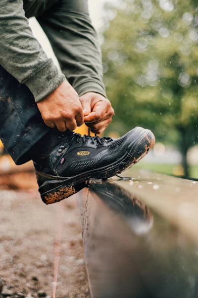 Muddy black work boot being tied with blurred outdoor background