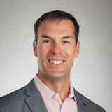 Smiling professional in gray suit and pink shirt against neutral background