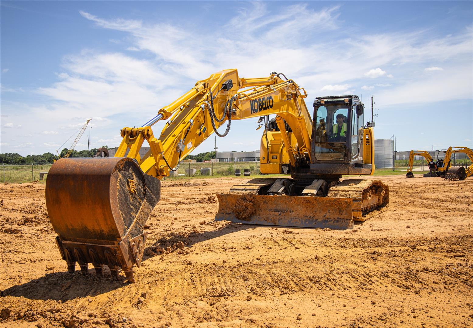 Yellow Kobelco excavator working on sandy construction site with blue sky