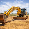 Yellow Kobelco excavator working on sandy construction site with blue sky