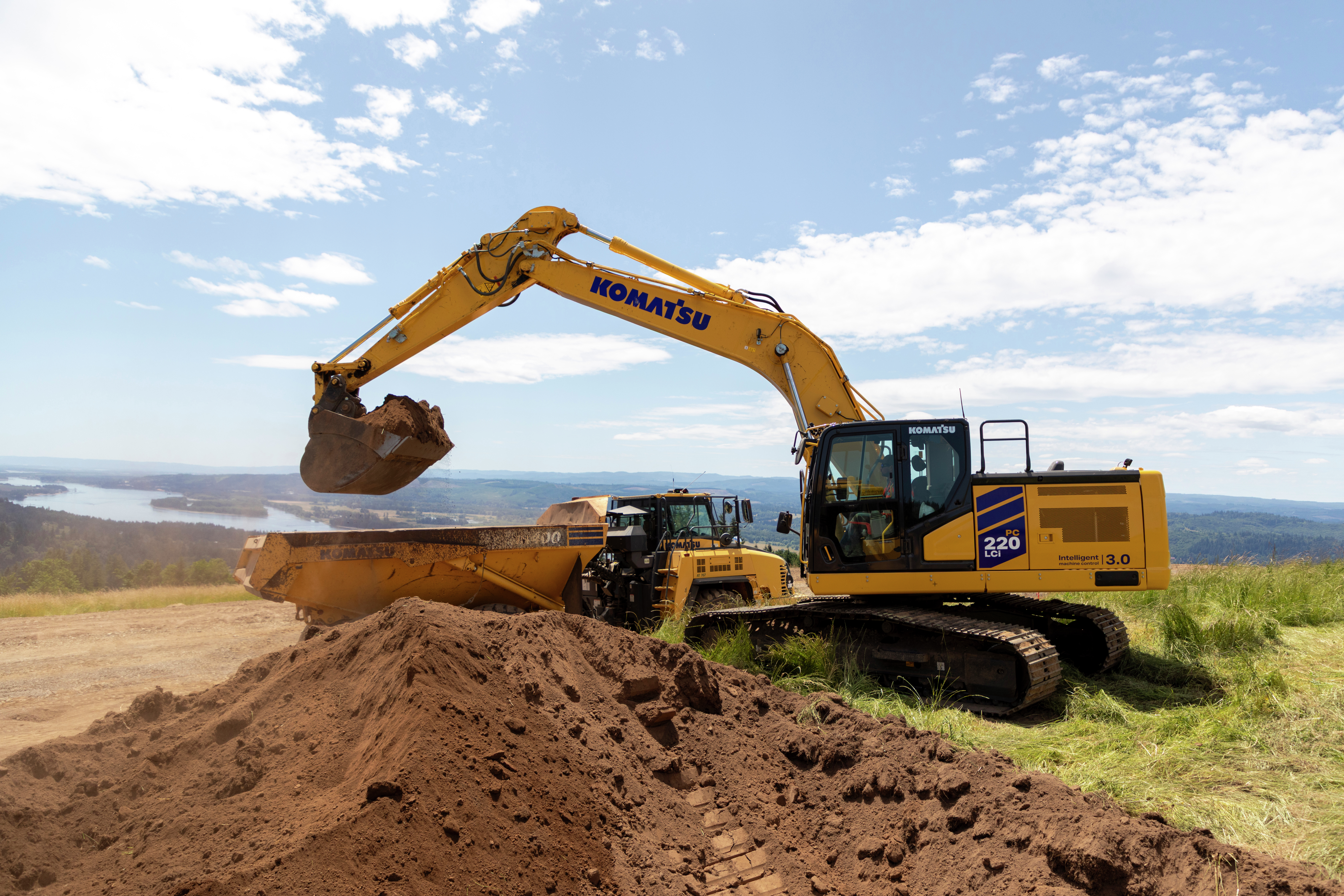 Yellow Komatsu excavator loading soil at construction site with dump truck