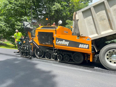 Orange LeeBoy 8680 asphalt paver machine laying fresh black pavement near trees