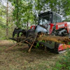 Red Manitou forestry machine moving fallen tree logs in wooded forest area