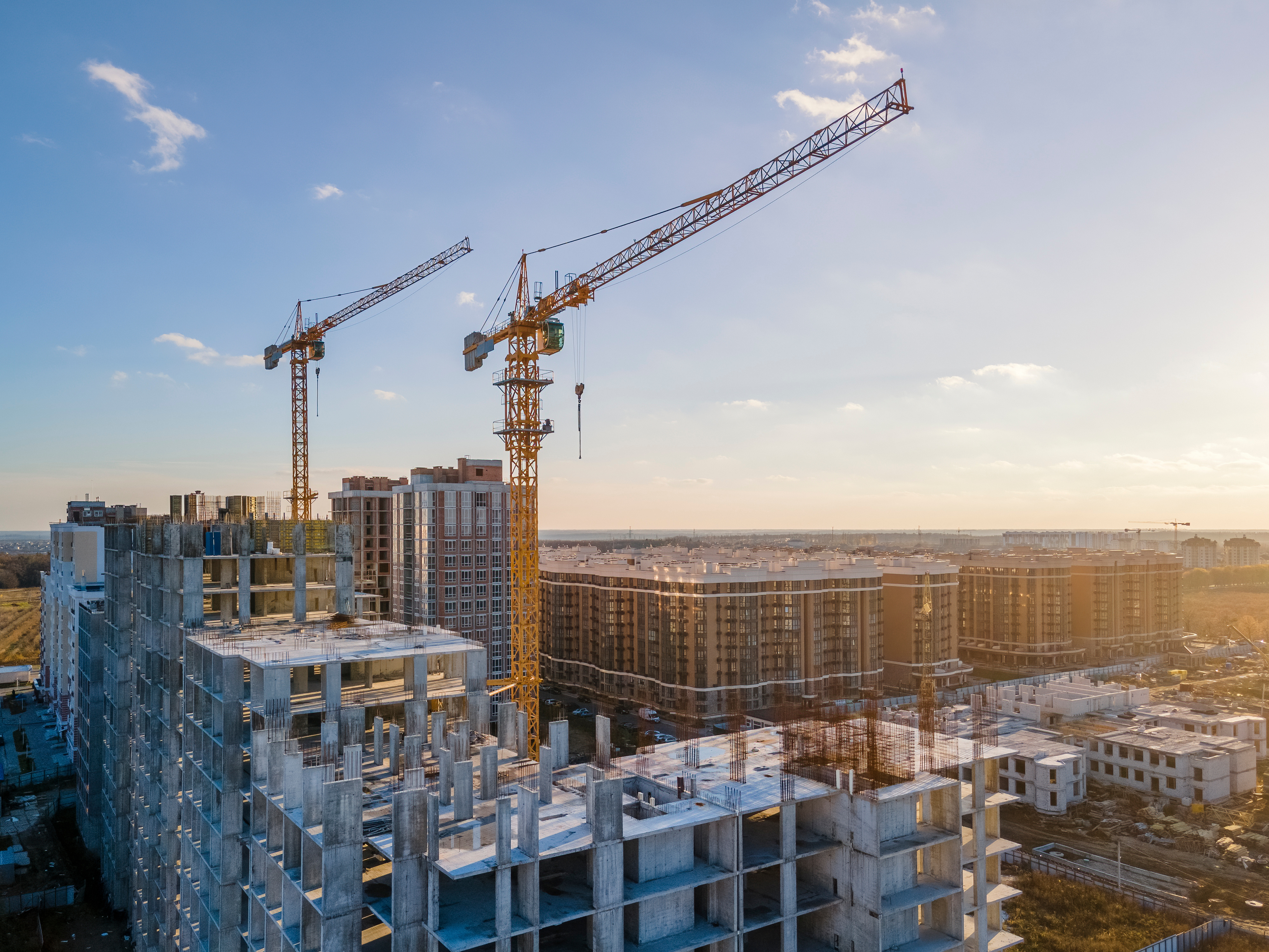 Urban construction site with high-rise buildings and yellow tower cranes at sunset