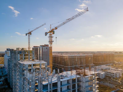 Urban construction site with high-rise buildings and yellow tower cranes at sunset