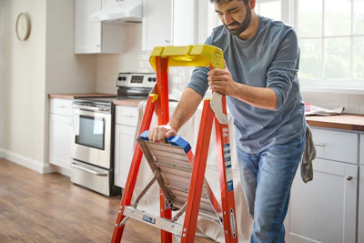 Person using a red ladder to work in a kitchen with stainless steel appliances