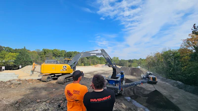Construction workers observing excavator and paving equipment on job site