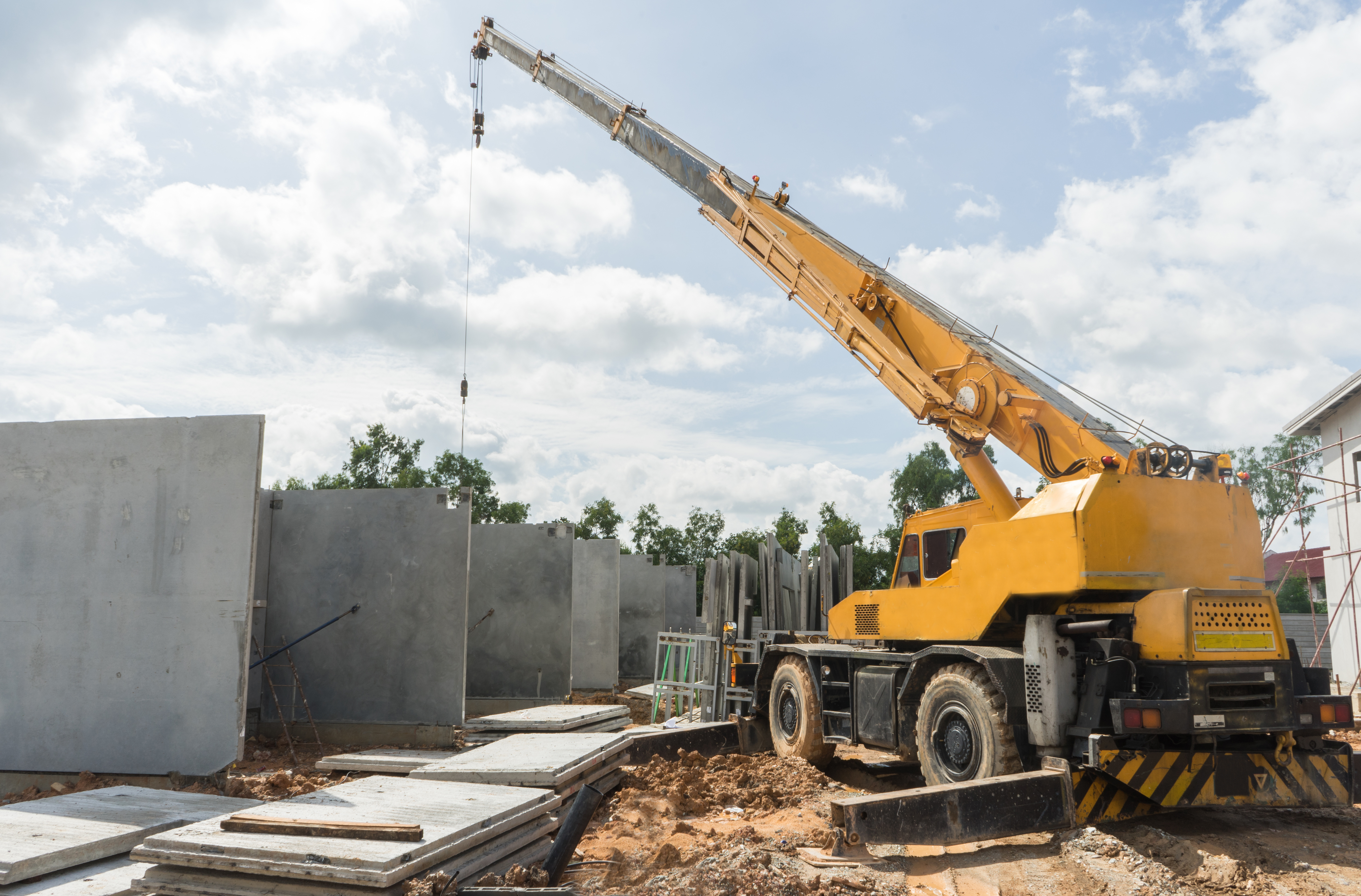 Yellow mobile crane positioned near concrete wall panels at construction site