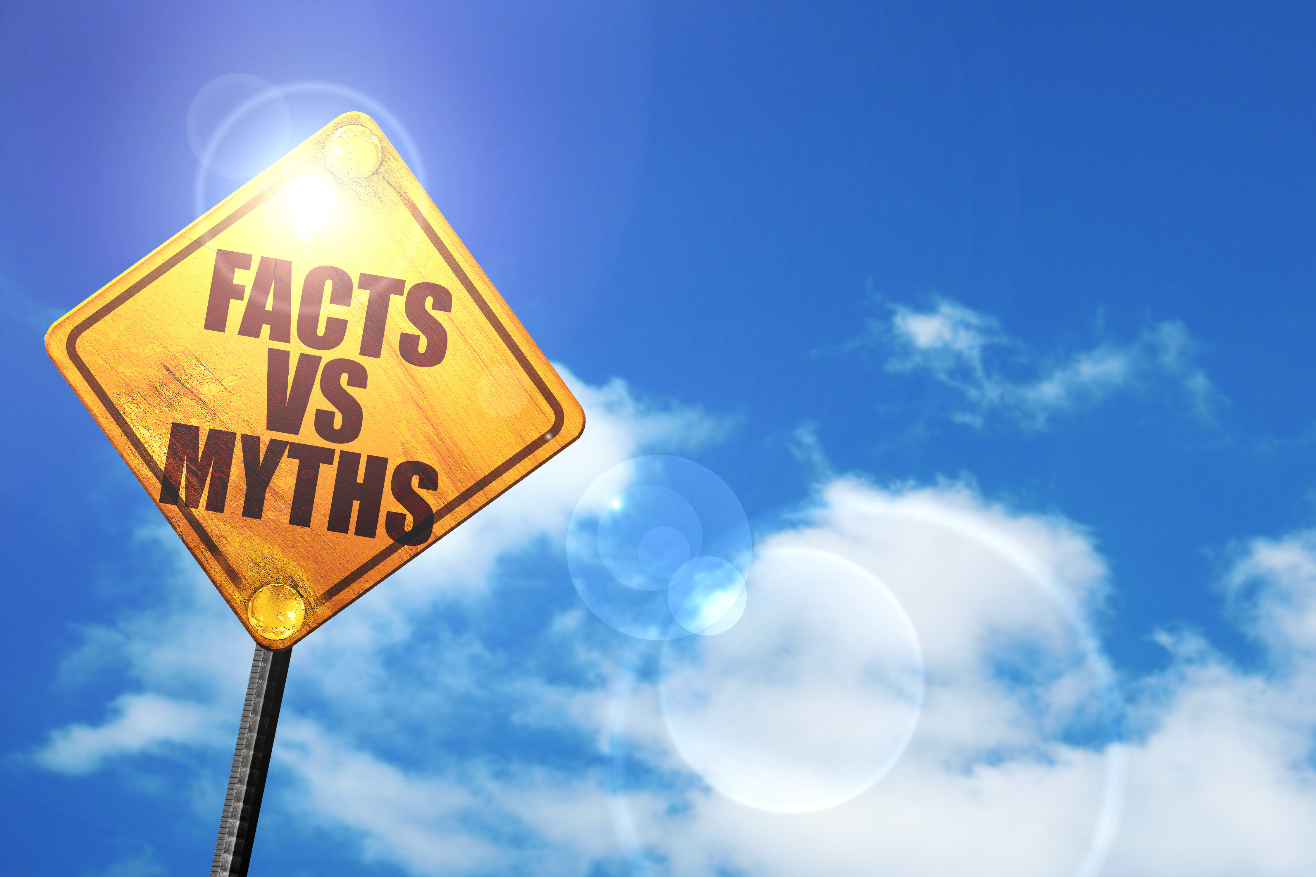 Yellow road sign reading 'Facts vs Myths' against bright blue sky with clouds
