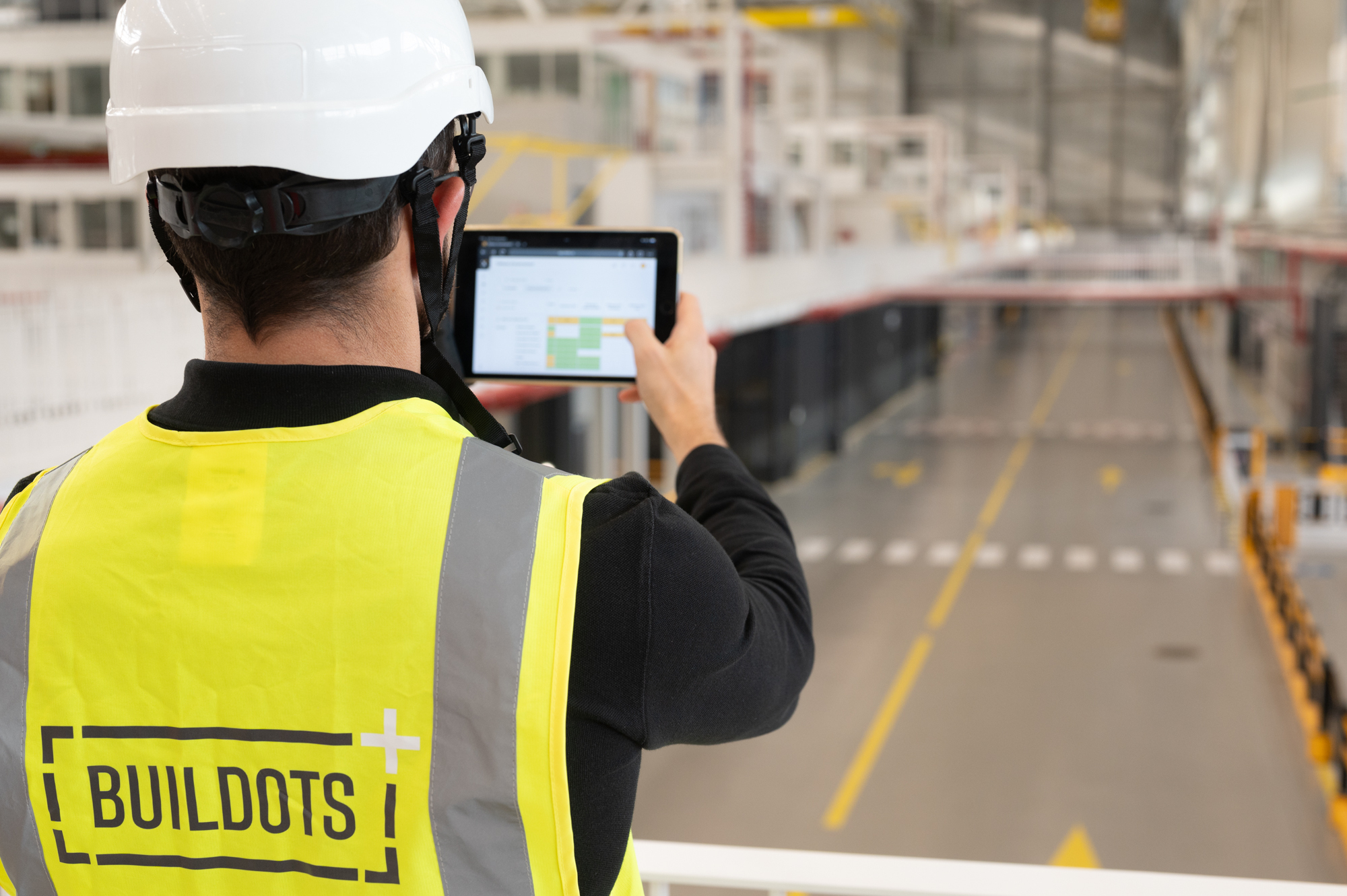 Construction worker in safety vest with Buildots logo using tablet on site