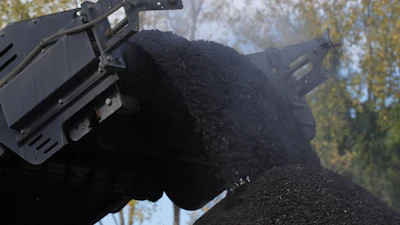 Industrial excavator dumping dark material against autumn tree backdrop