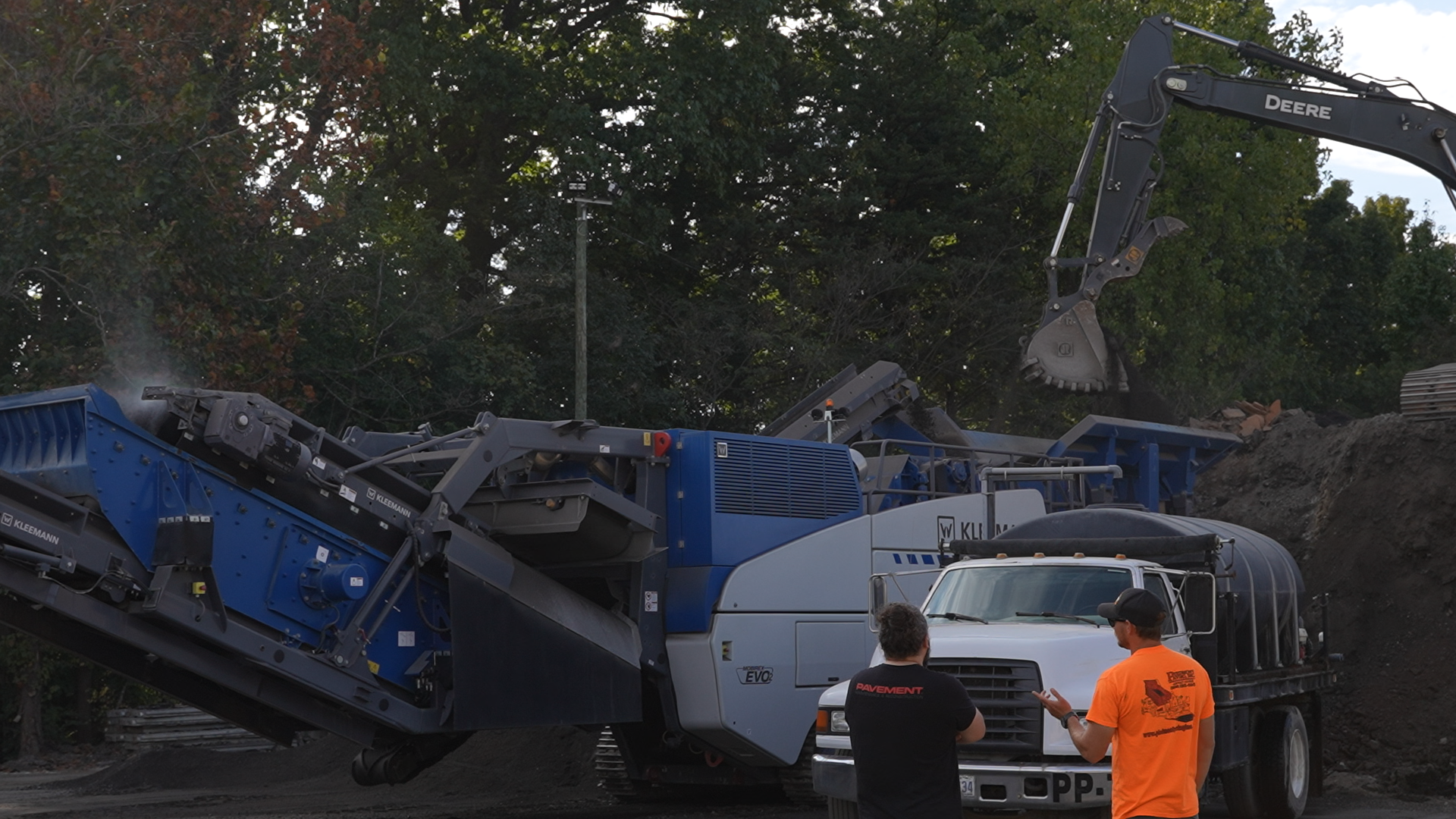 Construction site with blue excavation machinery and workers in orange safety vest