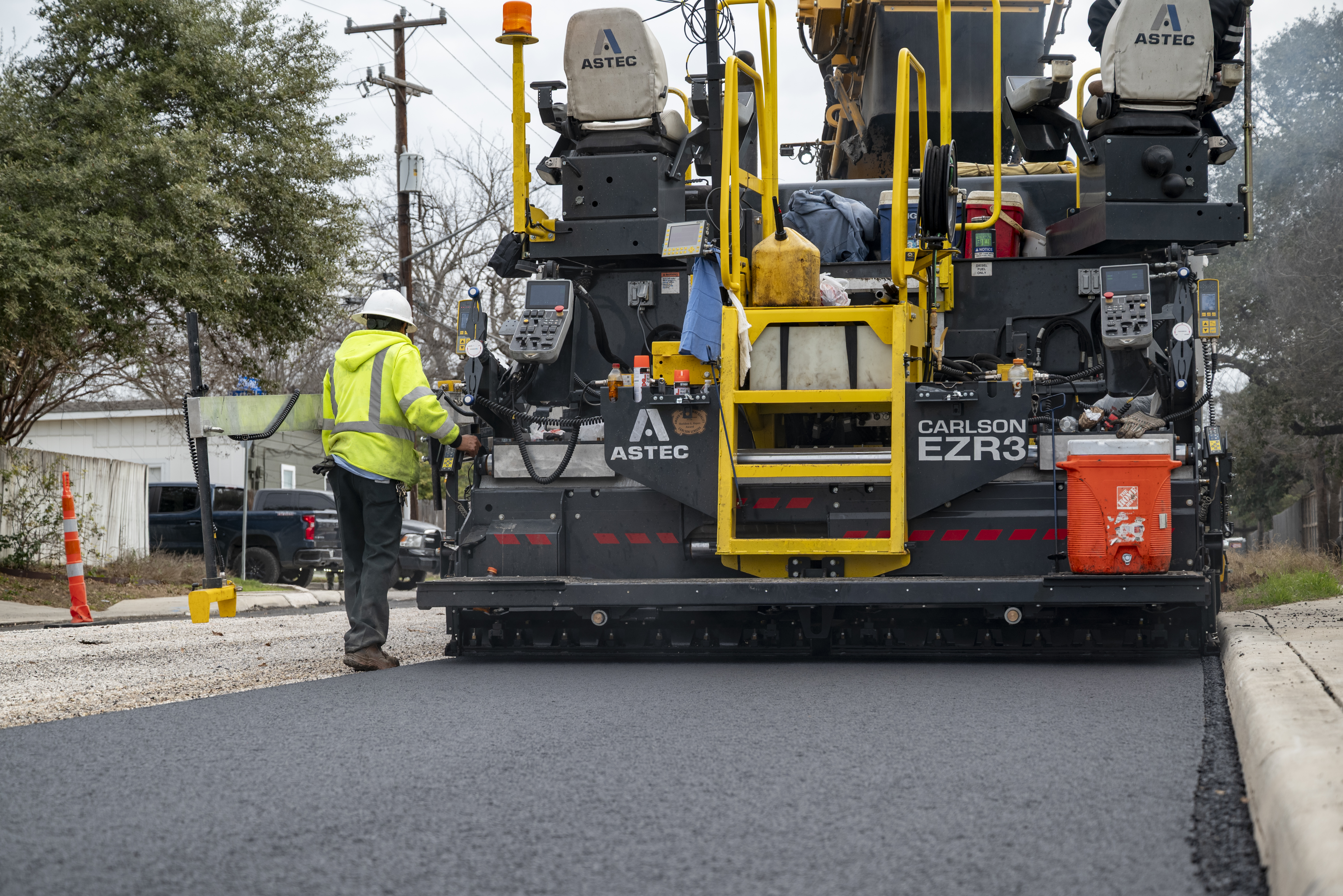 Road paving machine laying fresh asphalt on urban street with worker in safety vest