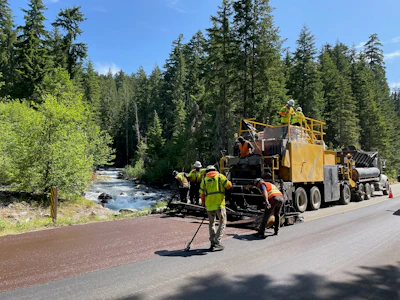 Road paving crew working beside a forest stream on a sunny day