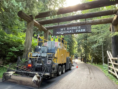 Yellow road paving truck at Mt. Rainier National Park entrance sign in forest setting