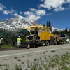 Yellow road paving machine working on highway near snow-capped Mount Rainier