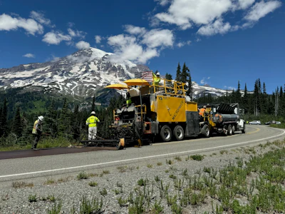 Yellow road paving machine working on highway near snow-capped Mount Rainier