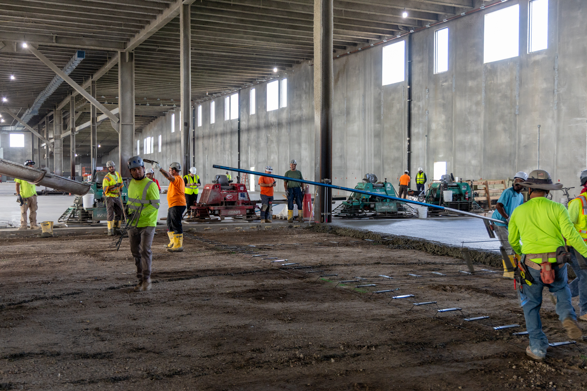 Construction workers in safety gear inside large industrial building with dirt floor
