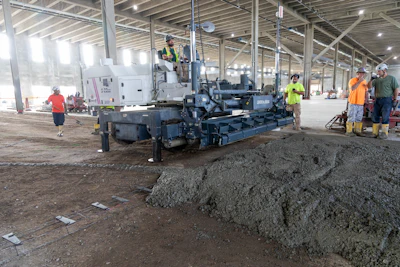 Construction workers operating concrete paving machine inside large industrial building