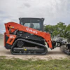 Orange Kubota SVL skid steer loader with attachment on dirt ground