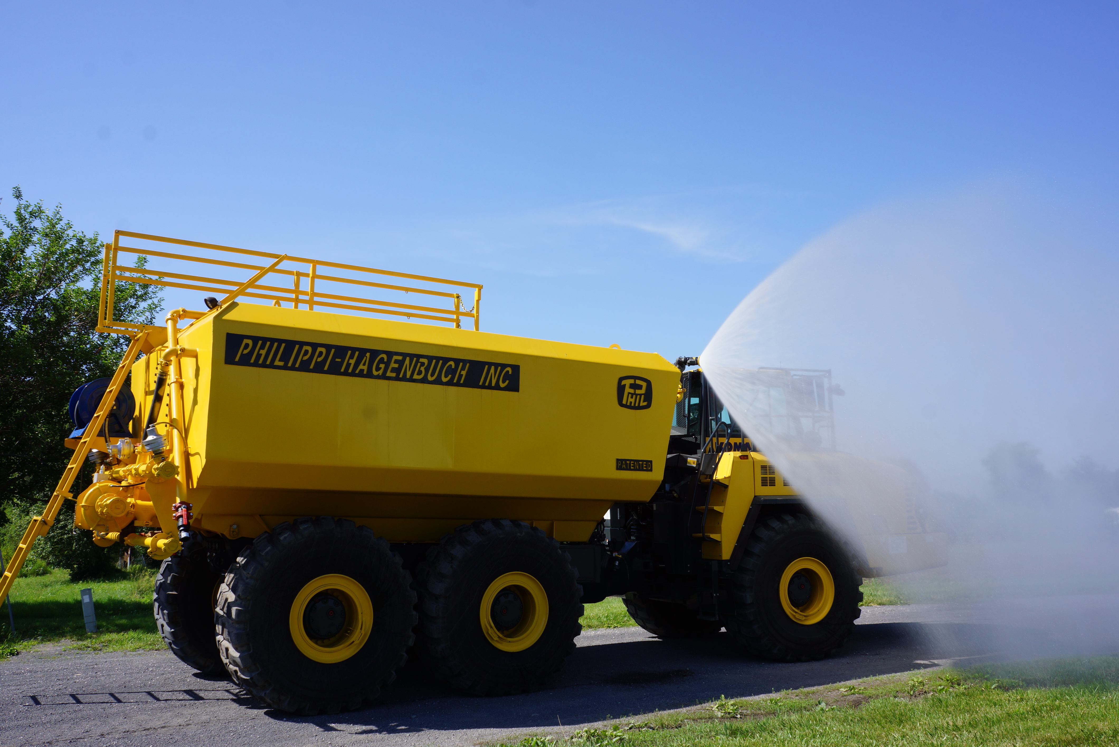 Large yellow industrial water truck by Philippi-Hagenbuch spraying water on pavement