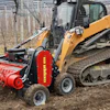 Yellow tracked skid steer with red forestry mulcher working in bare orchard