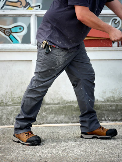 Worker wearing brown steel-toe boots and gray work pants on concrete surface