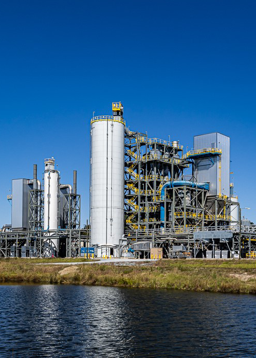 Industrial chemical processing plant with white tanks and metal structures near water