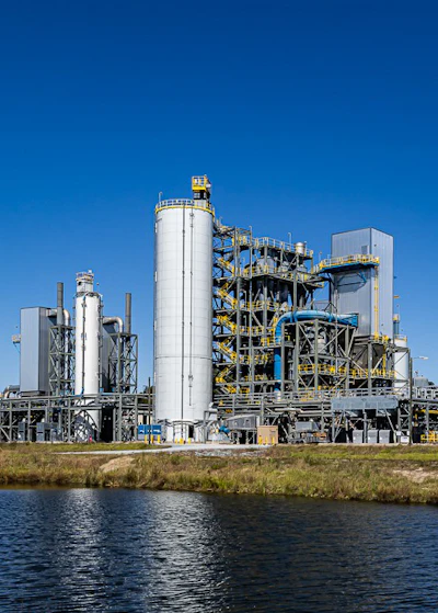 Industrial chemical processing plant with white tanks and metal structures near water