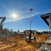Construction site with excavator, solar tower, and sandy ground under bright blue sky