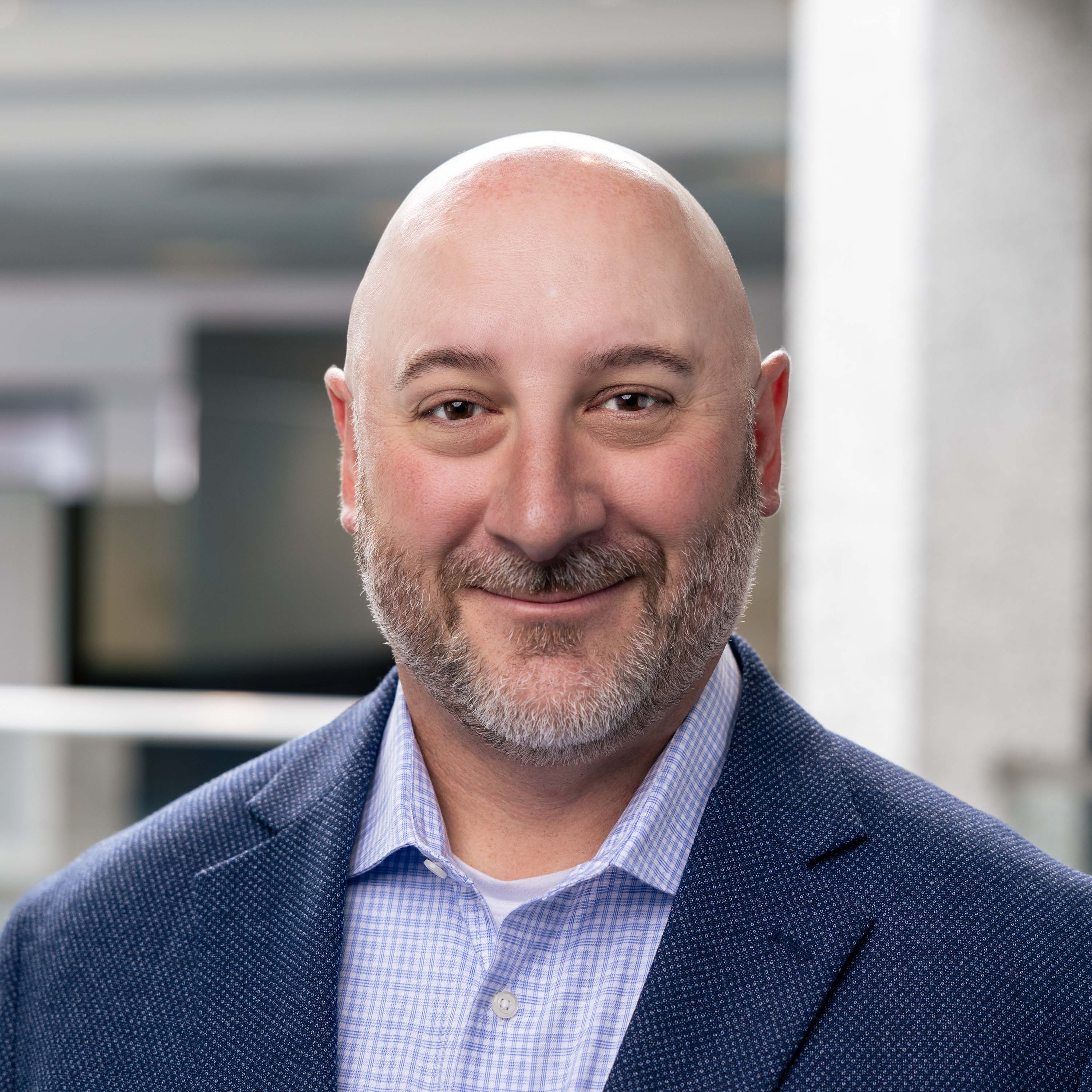 Smiling professional in navy blazer and checked shirt, bald with gray beard Headshot