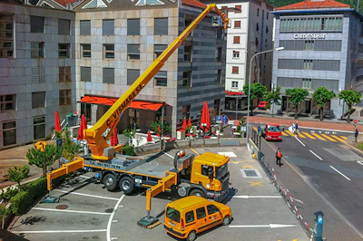 Yellow crane truck parked on urban street with red vehicles and surrounding buildings
