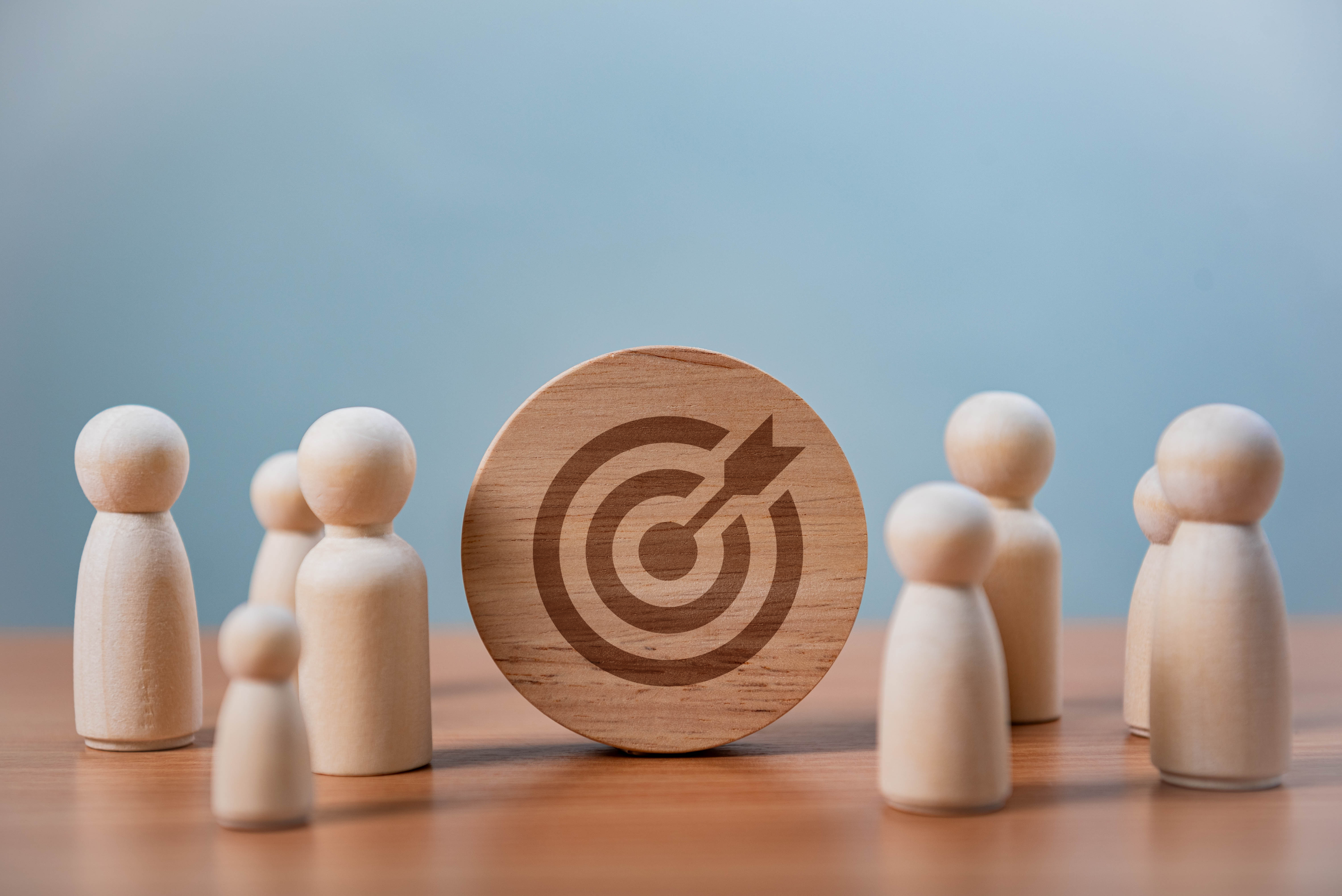 Wooden target icon surrounded by small wooden figurines on blue background