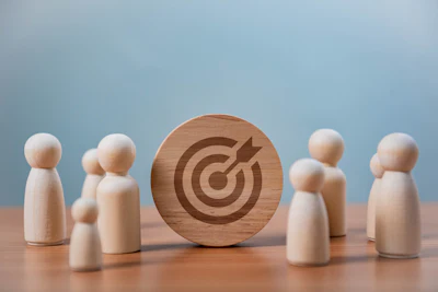 Wooden target icon surrounded by small wooden figurines on blue background