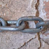 Gray metal chain links connected against weathered stone background