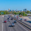 Multi-lane urban highway with vehicles, curving roadway and city skyline under blue sky