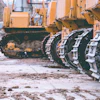 Yellow construction bulldozers with metal tracked wheels on muddy construction site