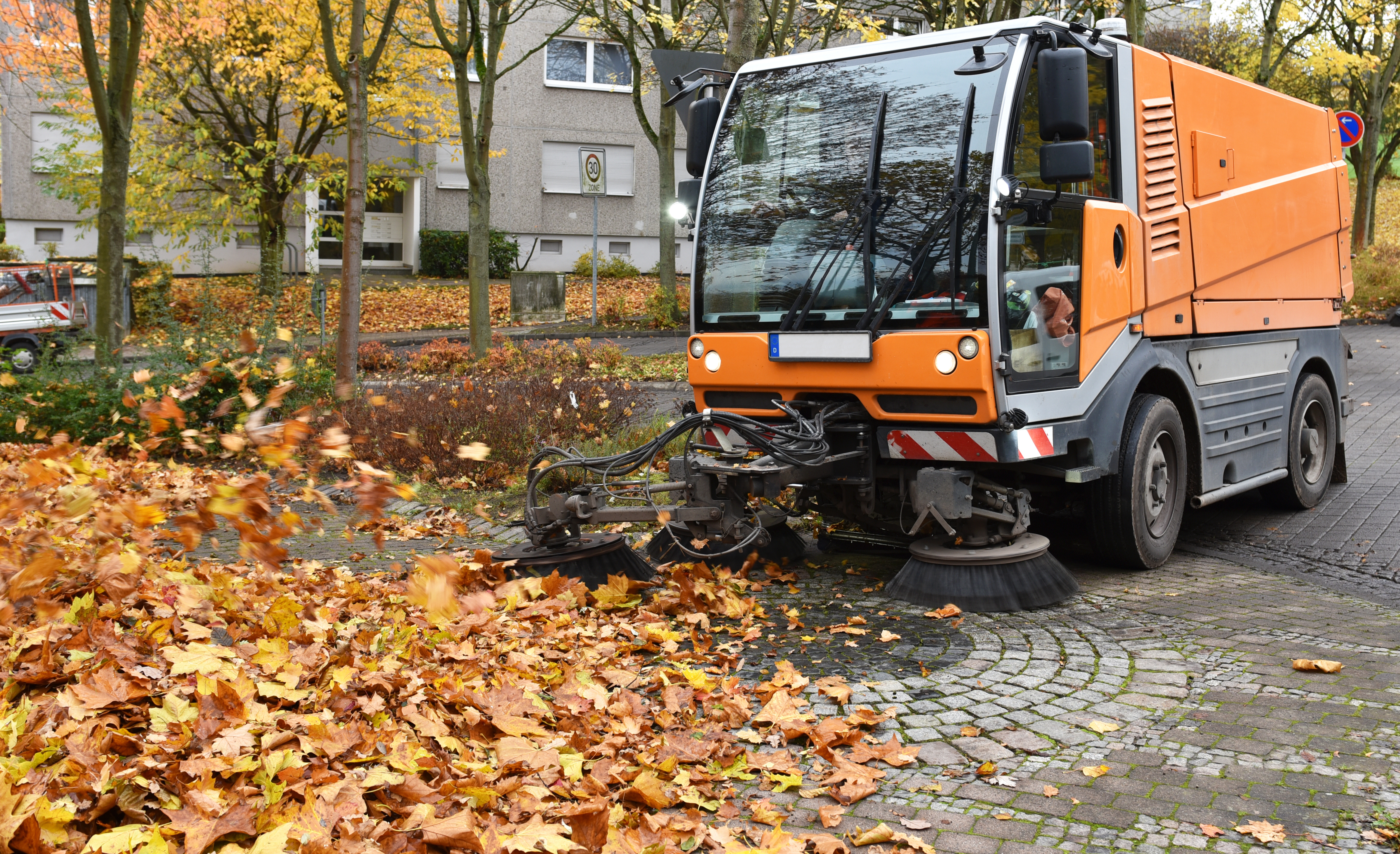 Orange street sweeper clearing fallen autumn leaves on cobblestone street