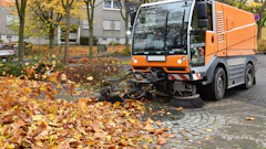 Orange street sweeper clearing fallen autumn leaves on cobblestone street