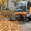 Orange street sweeper clearing fallen autumn leaves on cobblestone street