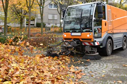 Orange street sweeper clearing fallen autumn leaves on cobblestone street