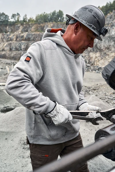 Construction worker in safety gear using tools at a rocky quarry site