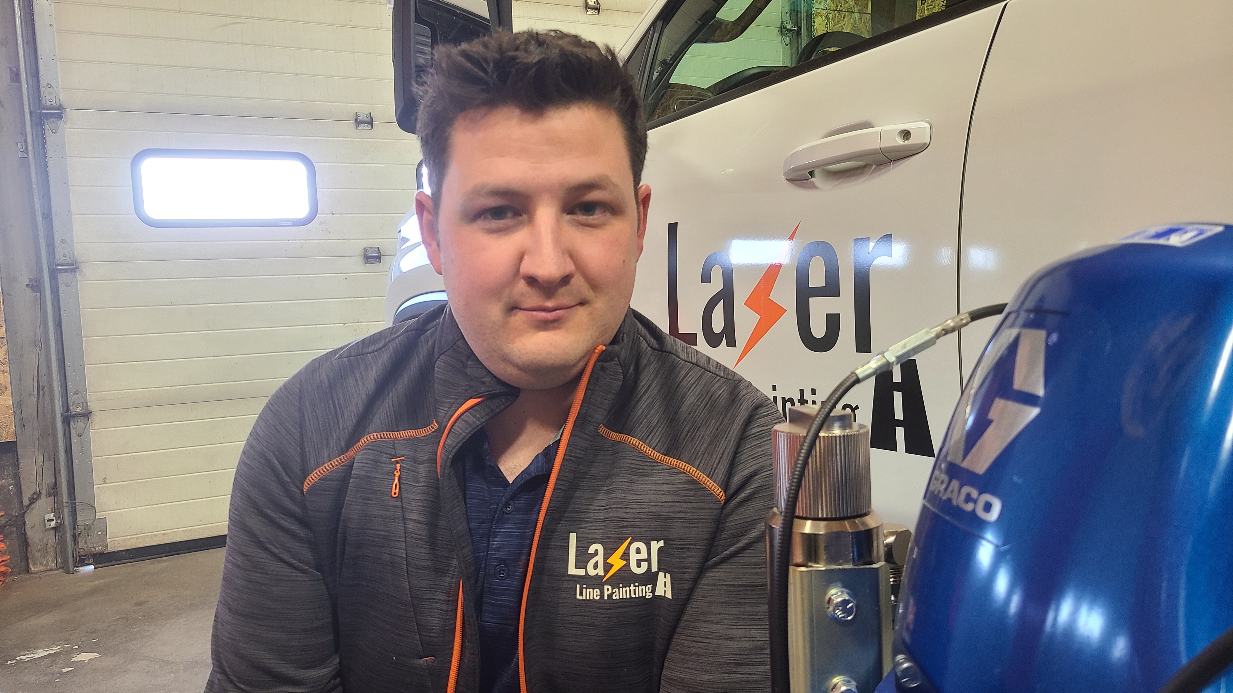 Lazer Line Painting employee in branded gray and orange uniform standing in garage